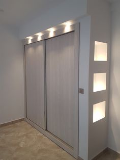 an empty room with two sliding doors and lights on the wall above them, in front of a white wall