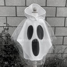 a white and black ghost costume sitting on top of a wooden pole next to a brick wall