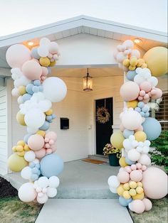 an arch made out of balloons in front of a white house with a black door