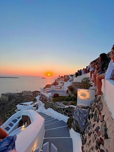 people sitting on the edge of a cliff watching the sun go down over the ocean