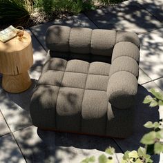 a gray couch sitting on top of a wooden table next to a tree stump and plant