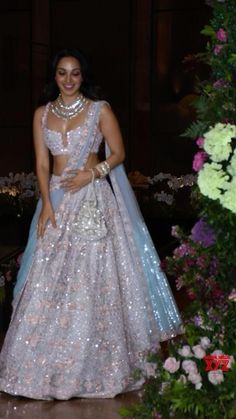 a woman in a white and blue lehenga standing next to some purple flowers