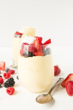 two glasses filled with fruit and ice cream on top of a white table next to spoons