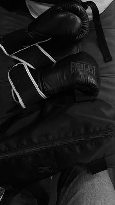 a pair of black boxing gloves sitting on top of a brown leather bag next to a man's leg