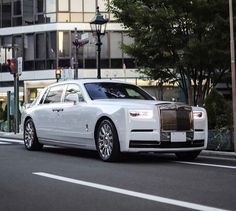 a white rolls royce parked in front of a tall building