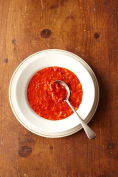 a bowl of tomato sauce with a spoon in it on a wooden table next to a plate