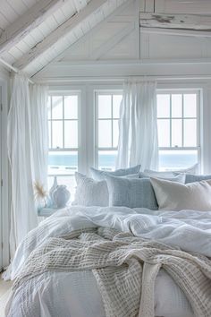 a bed with white linens and pillows in a room next to two large windows