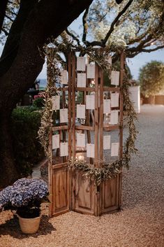 a wooden structure with pictures on it sitting next to a potted plant and tree