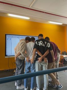 a group of young men standing in front of a large screen tv, with their arms around each other