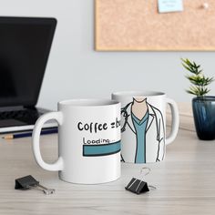 two coffee mugs sitting next to each other on a table with a laptop in the background