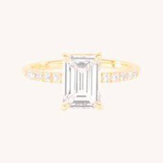 an emerald cut diamond ring set in yellow gold with diamonds on the shoulders and sides