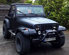 a black jeep is parked in front of some bushes