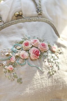 an embroidered purse with pink roses on it sitting on a white cloth covered bed sheet