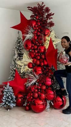 a woman standing next to a christmas tree with red and silver ornaments on it's sides