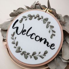 a white embroidered welcome sign surrounded by leaves