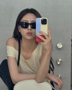 a woman wearing sunglasses taking a selfie with her cell phone while sitting on a chair