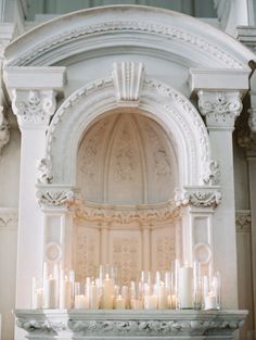 candles are lit in front of an ornate fireplace