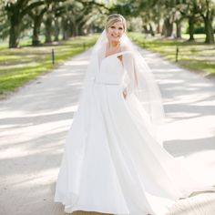 a woman in a white wedding dress standing on a path with trees and grass behind her