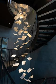 a spiral staircase with paper flying from the ceiling and lights hanging down on it's sides