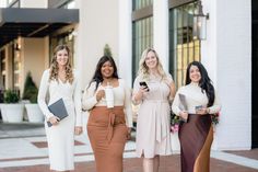 four beautiful women standing next to each other in front of a building holding notebooks