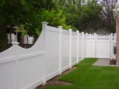 a white picket fence in front of a brick house with green grass on the side