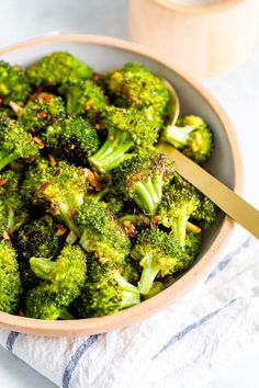 a bowl filled with cooked broccoli on top of a white towel next to a wooden spoon