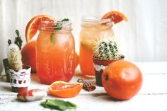 two jars filled with oranges and some other things next to each other on a table