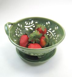 a green bowl filled with strawberries on top of a white table