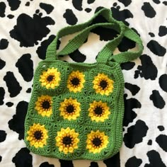 a green crocheted bag with sunflowers on the front and bottom, sitting on a cow print surface