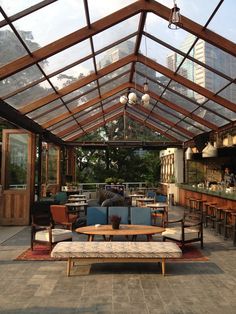 the inside of a restaurant with tables and couches under a glass roof over an outdoor dining area