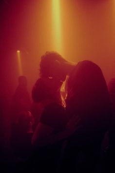 two people are standing in front of some bright lights at a concert or club with their backs to each other