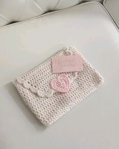 a white crocheted purse with a pink tag on it sitting on top of a couch