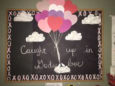 a chalkboard with balloons attached to it in front of a bulletin board that says caught up in love