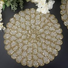 a gold doily sitting on top of a table next to white flowers and greenery