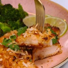 a pink plate topped with fish and broccoli next to a knife and fork