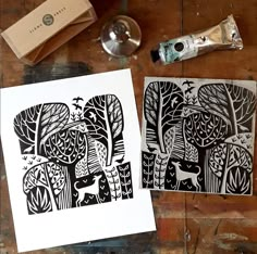 two black and white paper cut art pieces on top of a wooden table next to a tube of toothpaste