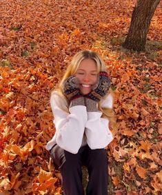 a woman is sitting in the leaves with her hands on her face and smiling at the camera