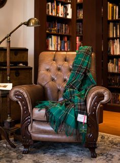 a chair with a plaid blanket on it in front of a book shelf filled with books