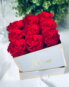 a bouquet of red roses in a white box with the word mom on it and gold lettering