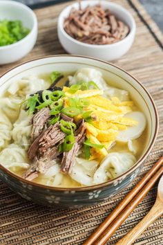 a bowl filled with noodles and meat on top of a table next to chopsticks