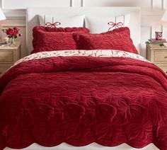 a red comforter set on a bed with white sheets and two nightstands in the background