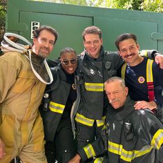 a group of men standing next to each other in front of a green wall wearing fire fighter gear