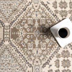 a cup of coffee sitting on top of a white and gray rug with an ornate design