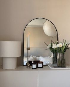 a white dresser topped with candles and vases on top of it next to a mirror