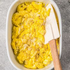 a white bowl filled with scrambled eggs and a wooden spatula