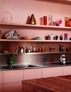 a kitchen with pink walls and stainless steel sink, shelves above the sink are filled with colorful dishes