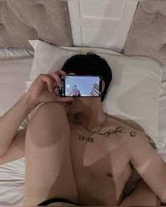 a shirtless man taking a selfie with his cell phone in the middle of bed