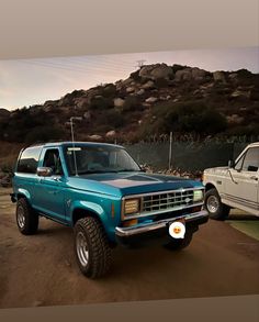 two pickup trucks parked in front of a mountain