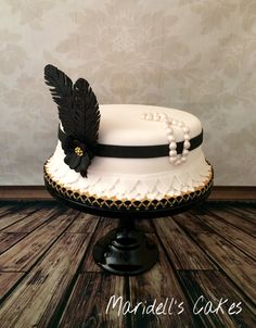 a white cake with black feathers and pearls on top sits on a pedestal in front of a wall