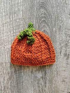 an orange knitted beanie with a green leaf on the top sits on a wooden surface